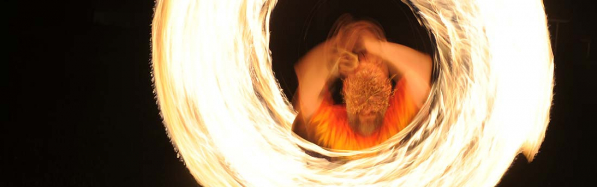 a man on an openwork metal greeenman mask spins fire at night