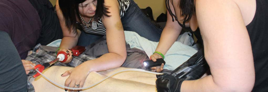 a group of women with stunguns and zipties pin someone to a bed