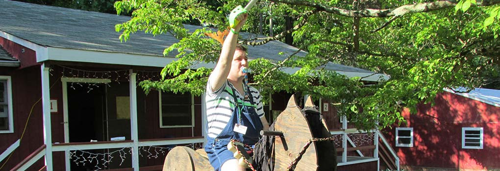 a male age-player in overalls, riding a giant rocking horse, while weiding a foam sword