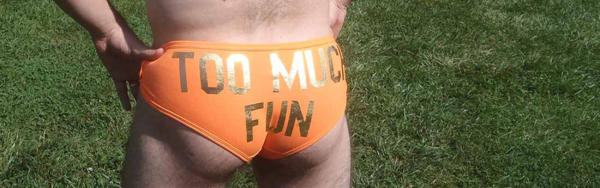 back view of a slender man in tight orange briefs, with "too much fun" in gold letters across the butt