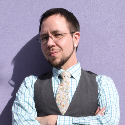 A sharply dressed man with a serious expression leans agains a purple wall